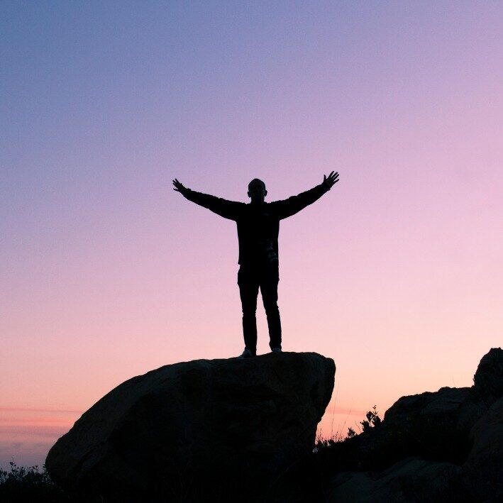 Purple and pink sunset with a man standing on a rock with arms in the air